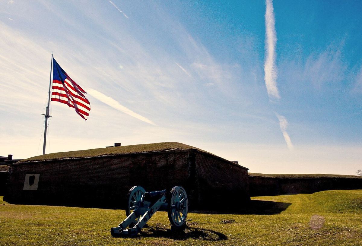 A cannon below the ramparts of Fort McHenry with the flag flying
